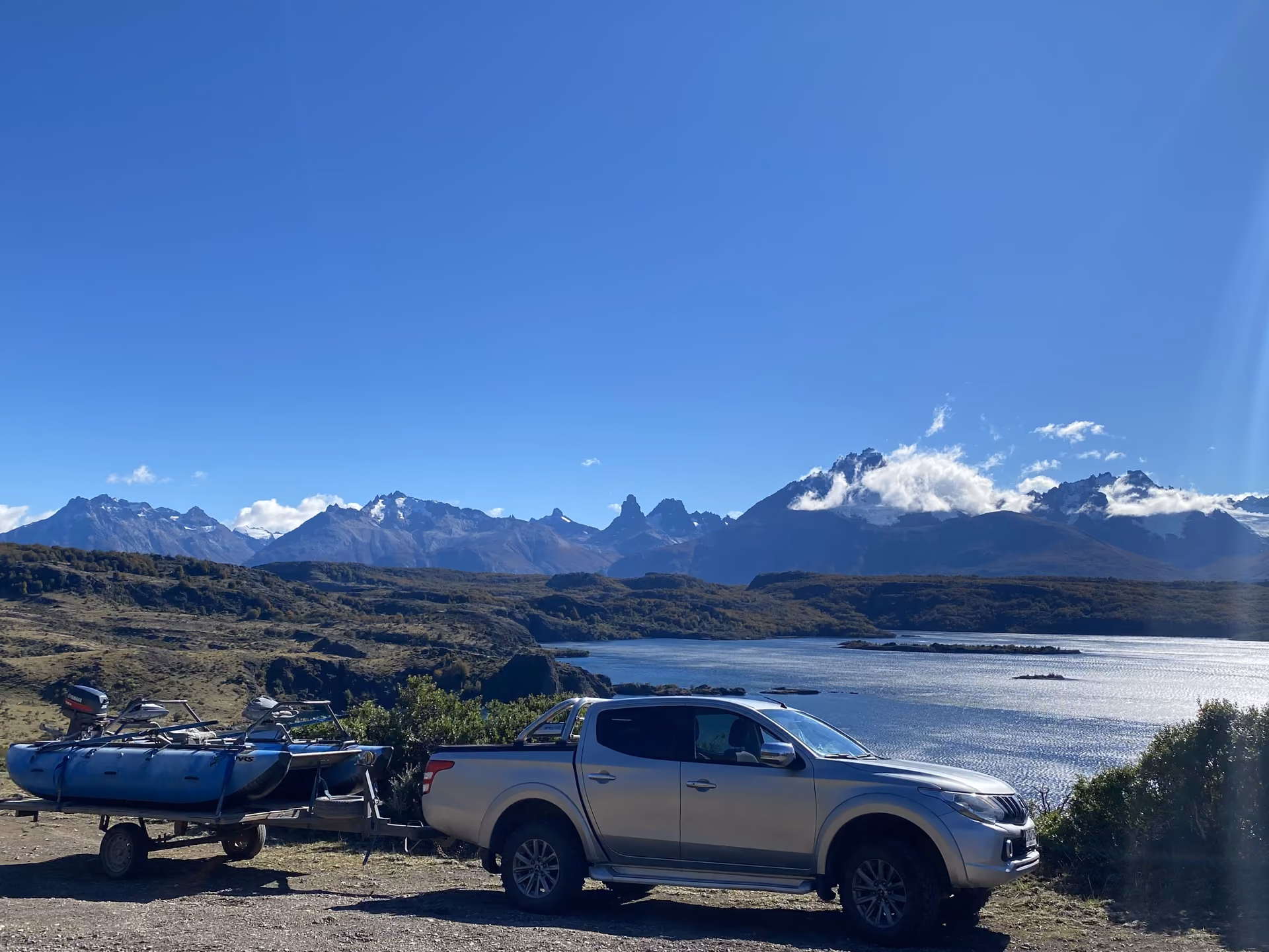 A 4x4 towing a cataraft above a lake in Chilean Patagonia, with snow-capped peaks behind