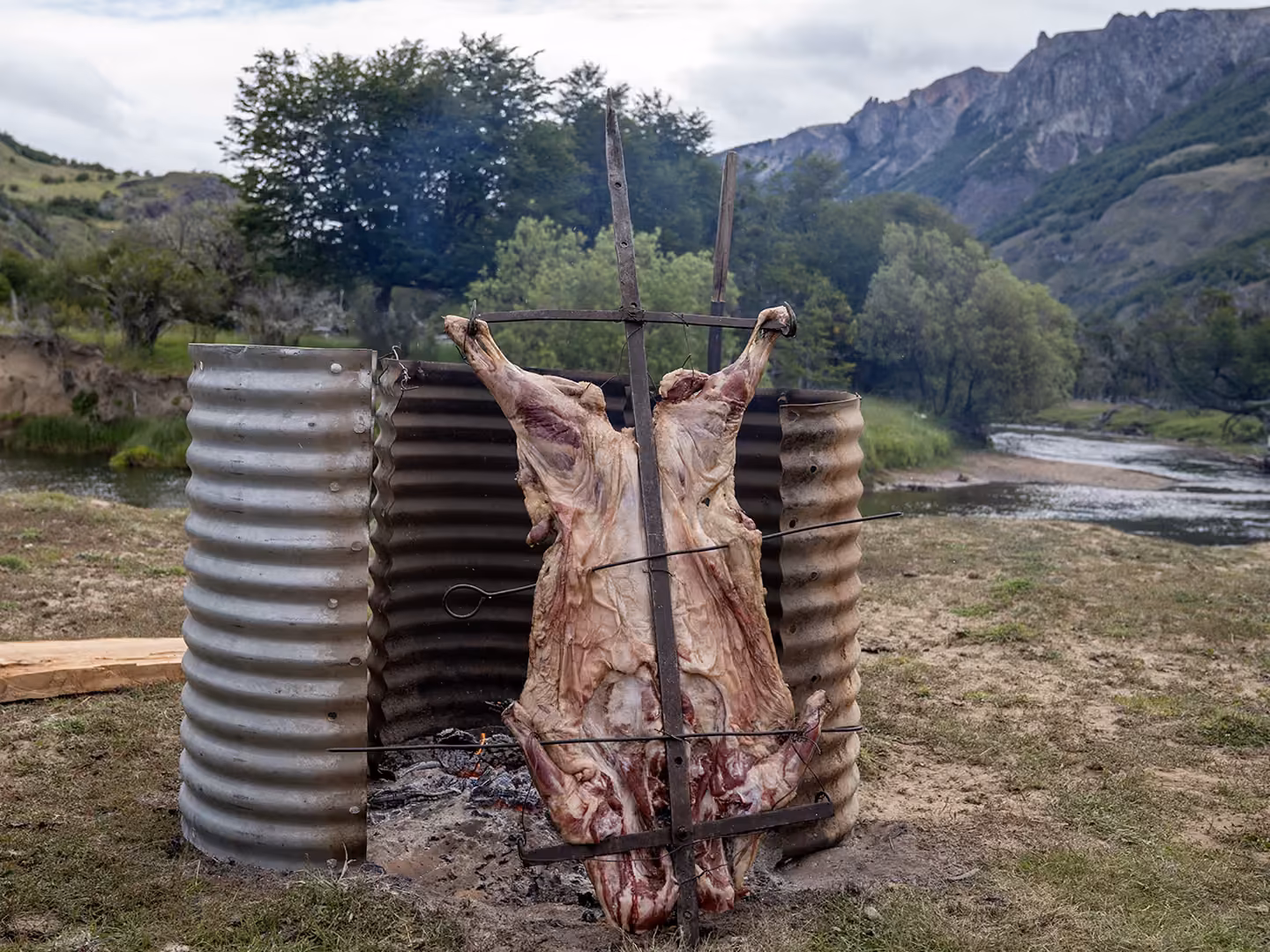 Lamb roasting over an open fire beside a river in Chilean Patagonia
