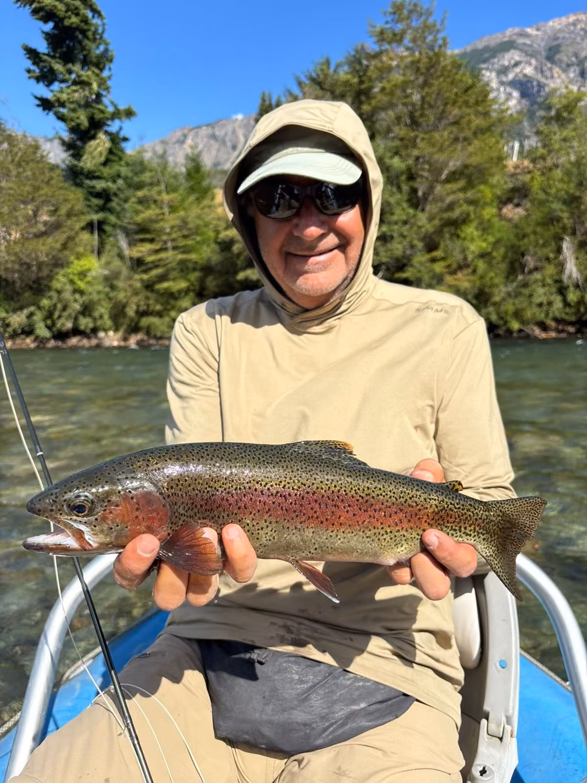 An angler with a rainbow trout in a boat on a forested river near Coyhaique, Chilean Patagonia