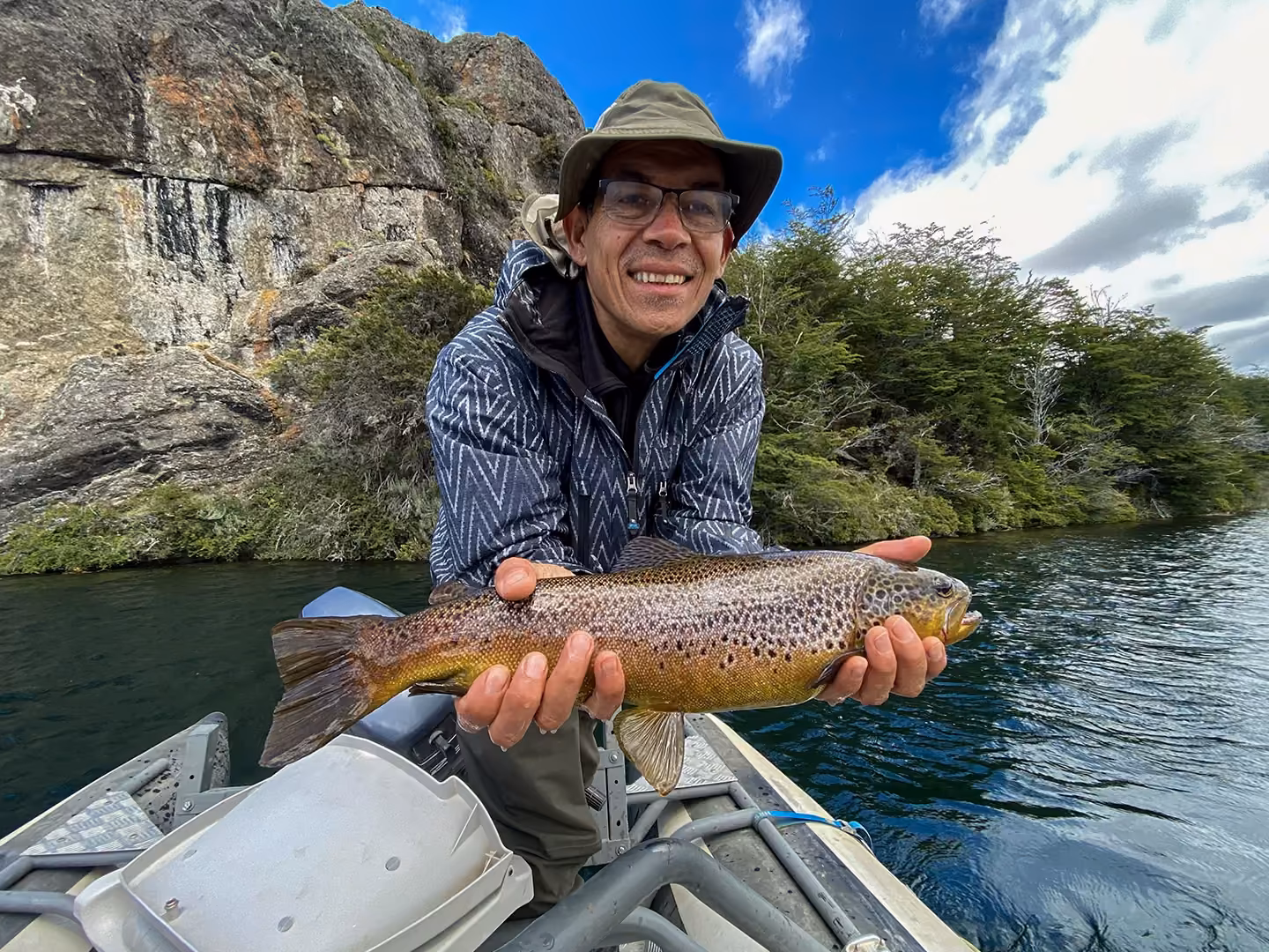 An angler holding a wild brown trout aboard the boat on a lake near Coyhaique