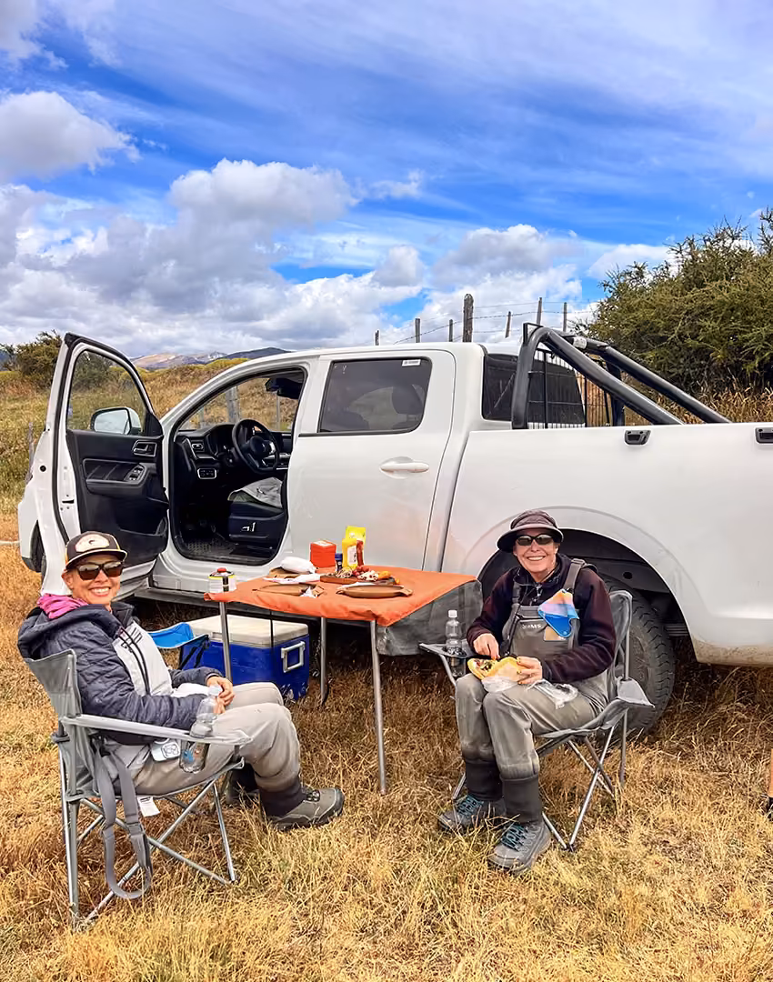 Two anglers at a riverside lunch table beside the guide's 4x4 near Coyhaique