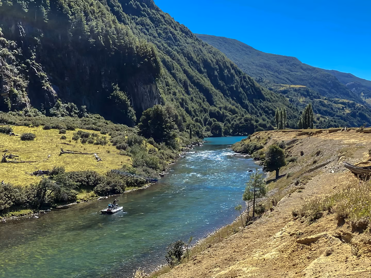 Anglers on a clear blue river between forested mountains near Coyhaique, Chilean Patagonia